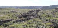 Vista geral da entrada à montante da Gruta, próxima ao sumidouro do Rio Lapão. A boca está posicionada na base do paredão. Este local se caracteriza como uma dolina de abatimento, onde o colapso do teto da cavidade formou um vale fechado. Ao fundo, é possível observar as escarpas das Serra do Sobradinho e Lapão (Foto: Nuno M. Martinho Vieira).