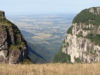 Perfeita tabularidade das rochas vulcânicas marcada no Cânion Malacara. A imagem mostra  o contato entre os derrames vulcânicos na forma de  degraus que se encontram cobertos por vegetação arbustiva. Ao fundo é vista a cidade de Praia Grande (SC) e no horizonte, a linha costeira catarinense e gaúcha. (Autor: Michel Godoy/2011)